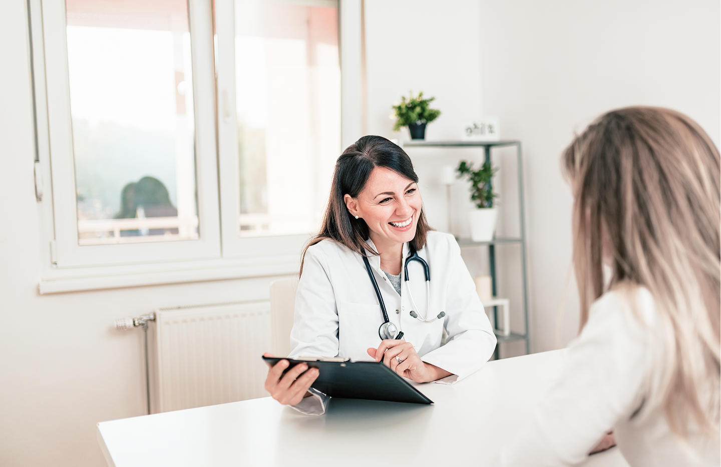 Female doctor smiling while speaking with a patient during a consultation in a medical office.