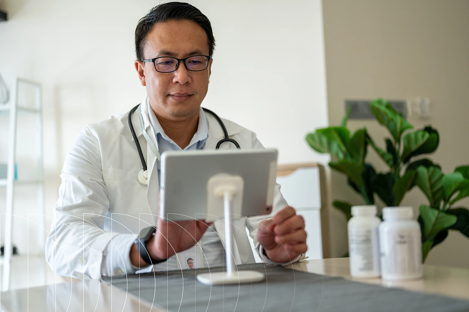 A doctor in his office interacts with a tablet sitting on his desk