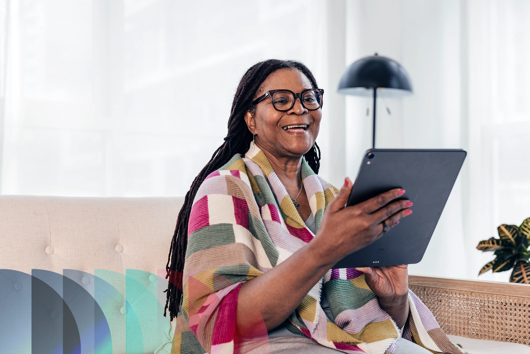 An older woman sitting on her couch at home smiles and interacts with her tablet