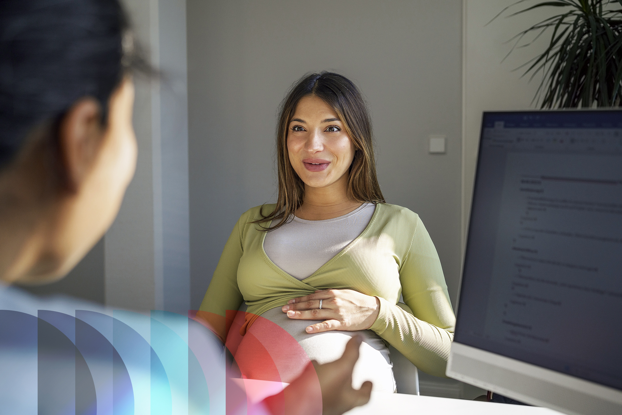 Pregnant patient smiling as she consults with a female gynecologist during a hospital clinic appointment.
