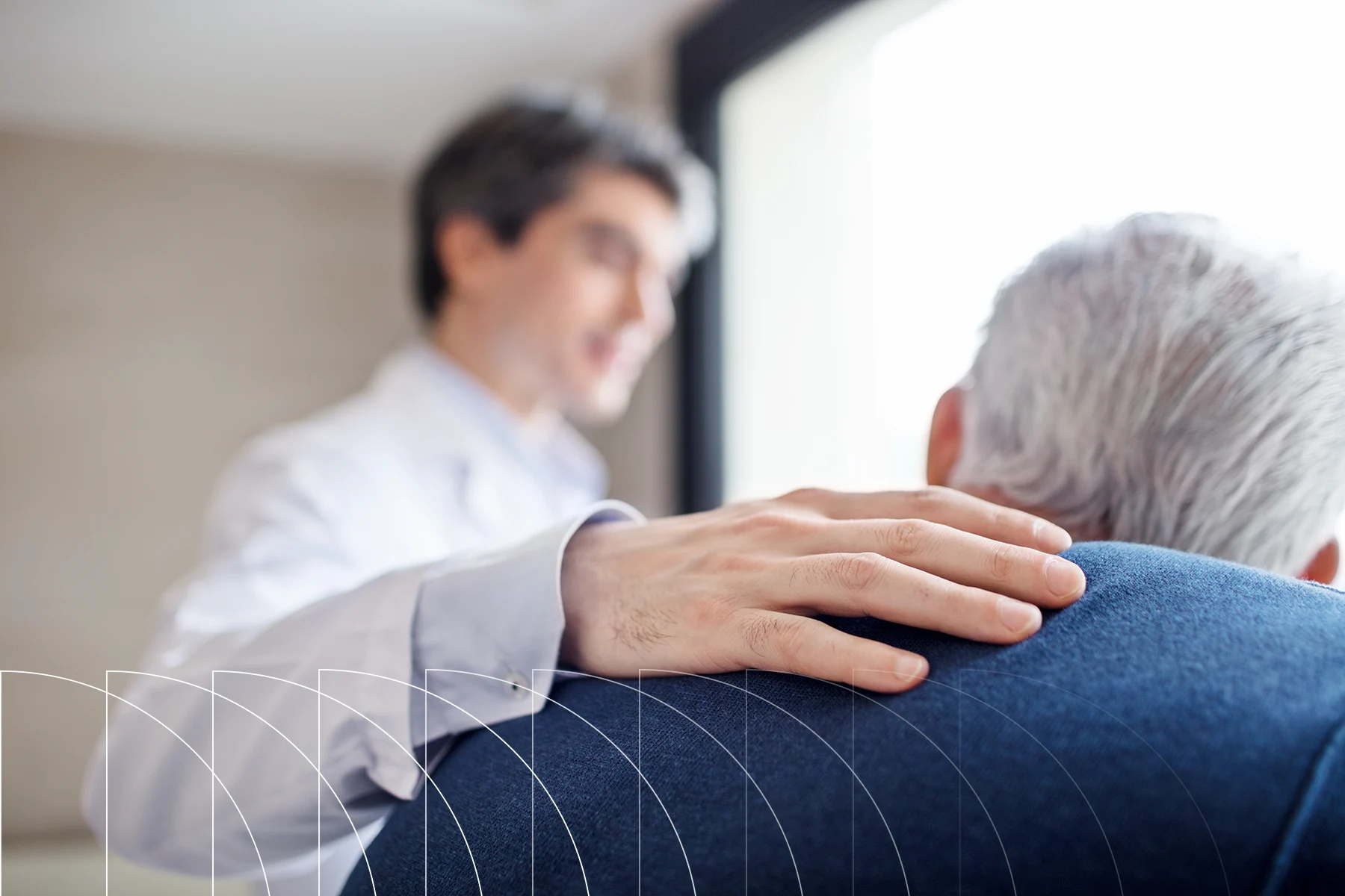 A doctor places a reassuring hand on a patient’s shoulder during a conversation.
