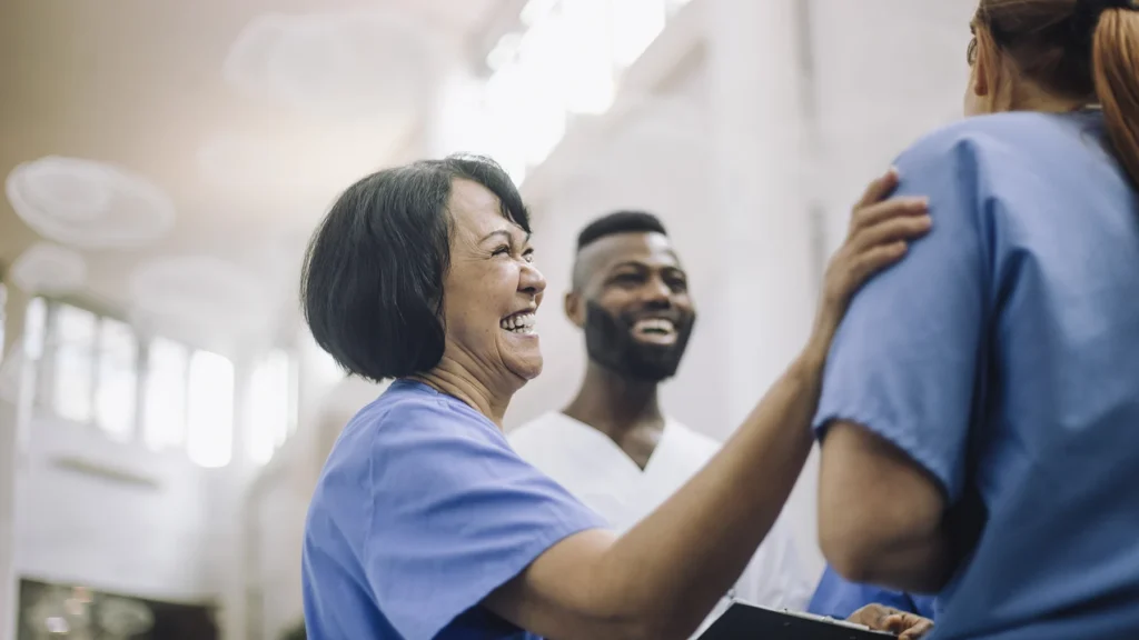 Side view of happy senior female doctor with hand on shoulder of colleague at hospital