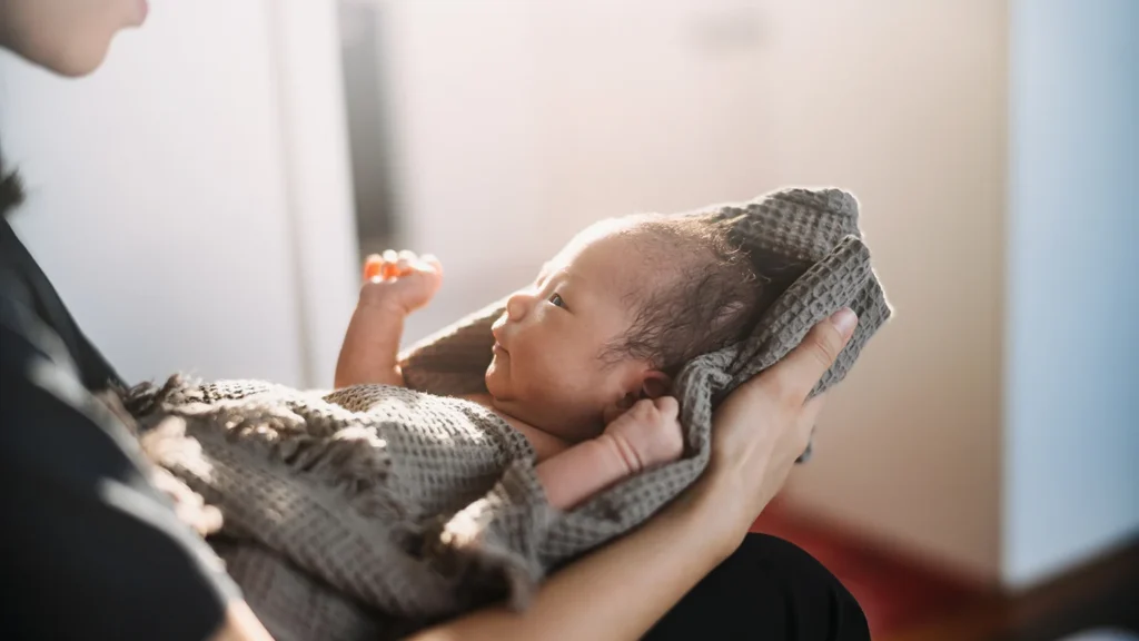 Cropped shot of a loving Asian mother holding newborn baby wrapped in a towel, drying baby girl after a fresh bath.