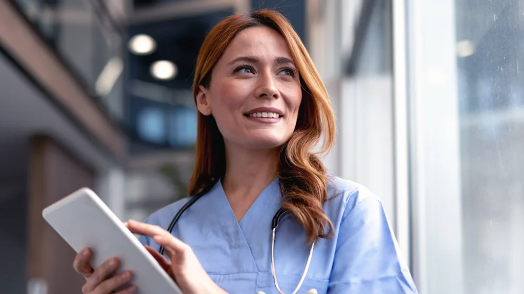 Smiling Healthcare Worker Using Digital Tablet Near a Window in a Modern Office