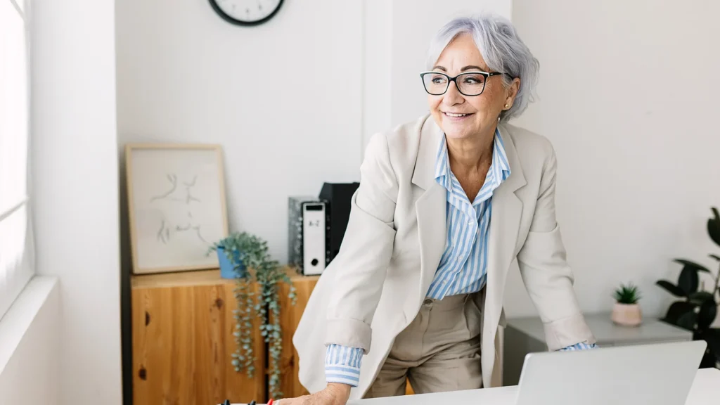 Happy mature middle aged businesswoman working on laptop computer at modern office workplace
