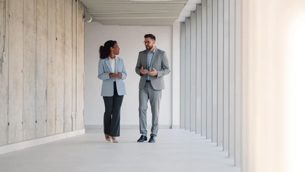 Two business professionals walk through a modern hallway while talking.