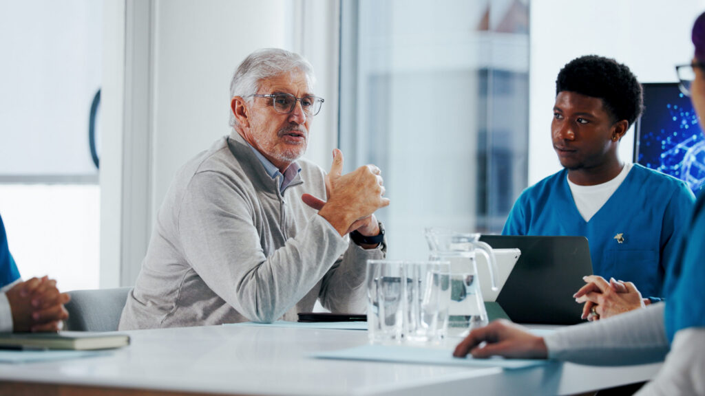 Healthcare professionals meeting with a senior clinician during a discussion in a clinical or office setting.